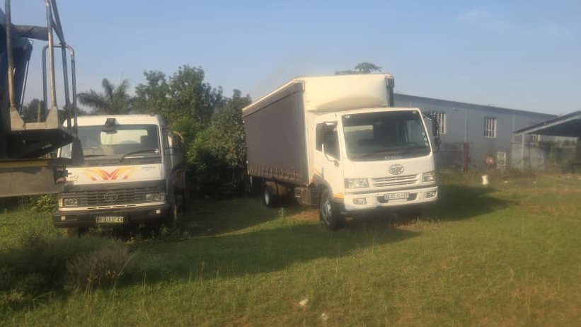 Medium duty commercial trucks: One of the trucks, on the left, is fitted with a flatbed body, while the other, on the right, is a curtain-side truck, designed for easy side loading and unloading of goods. Both vehicles are in fair condition. 